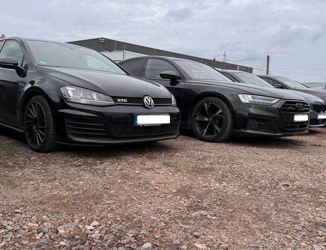 Prime Parking Valet - Kilka czarnych aut stoi na żwirowym placu. Samochody są zaparkowane blisko siebie. W tle widoczny jest płot i budynek.