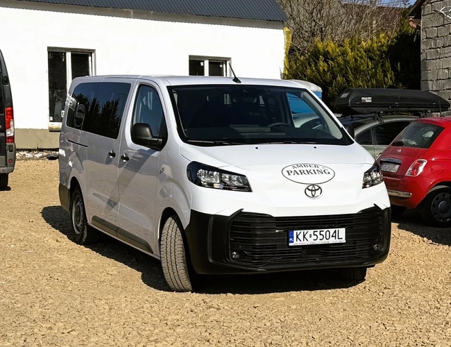 Parkovisko Amber — Na parkovisku stojí biele dodávkové vozidlo. Na pozadí sú viditeľné ďalšie vozidlá a budova.