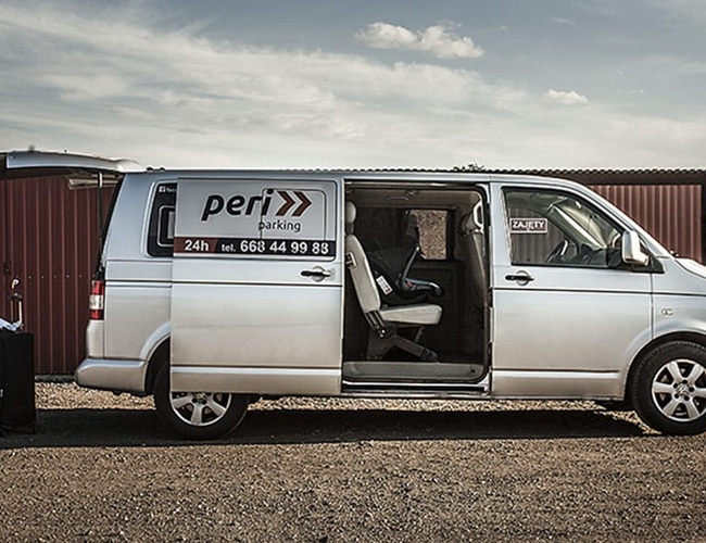 PERI Parking Garaże Premium – Srebrny van stoi na żwirze. Drzwi boczne są otwarte. Obok znajduje się walizka.