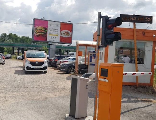 Orange Parking P3 – Teren jest utwardzony i ma szlaban. Widzimy zaparkowane auta i budkę z obsługą. Obok stoi znak drogowy.