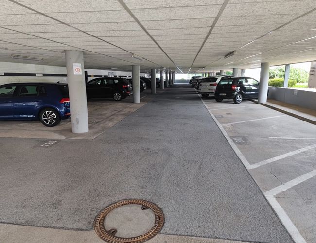 Parking FrankfurtValet24 - Zadaszony parking z miejscami postojowymi. Samochody stoją w równych rzędach. Betonowe filary wspierają dach.