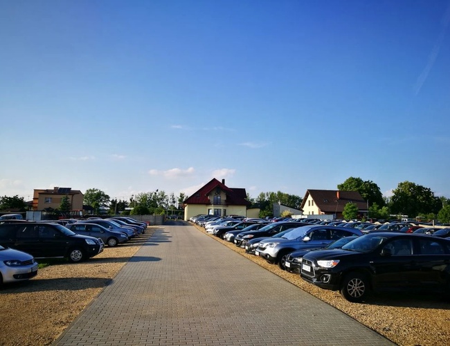 Aparcamiento Darex - Filas de coches están en un área pavimentada. Al fondo se pueden ver casas y árboles. El terreno es abierto y espacioso.