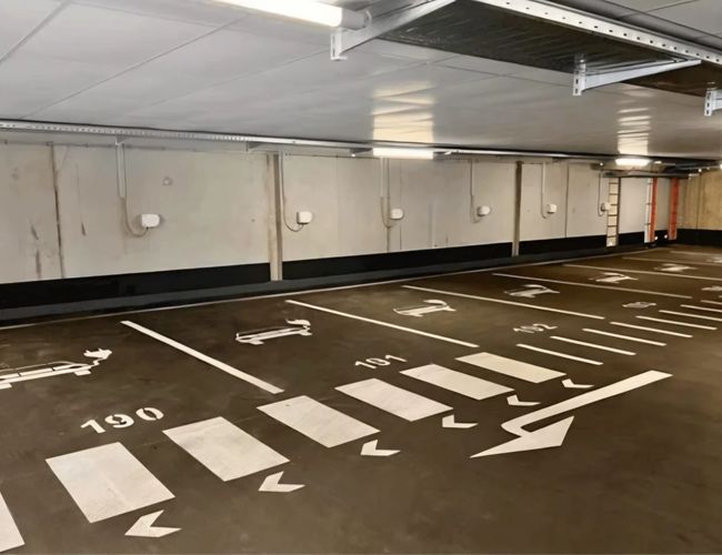 Parking Flughafenparker - Wnętrze podziemnego parkingu. Wolne miejsca są oznaczone numerami. Na podłodze widoczne są strzałki kierunkowe.