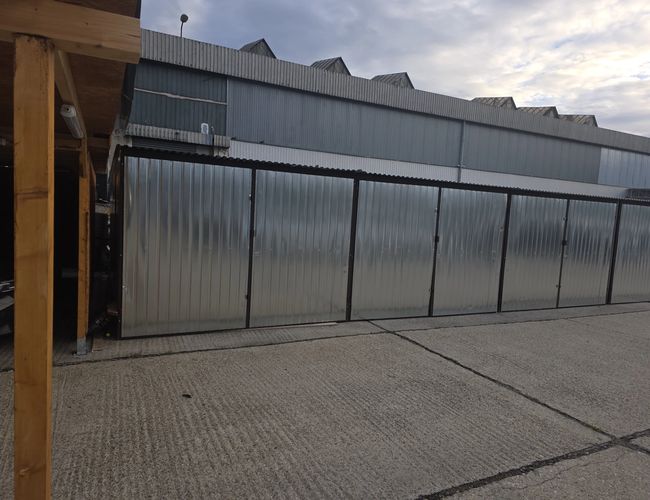Zadaszone stanowiska parkingowe PV Airport Parking w Bratysławie – drewniana wiata oraz zamykana konstrukcja z metalowych paneli na terenie parkingu