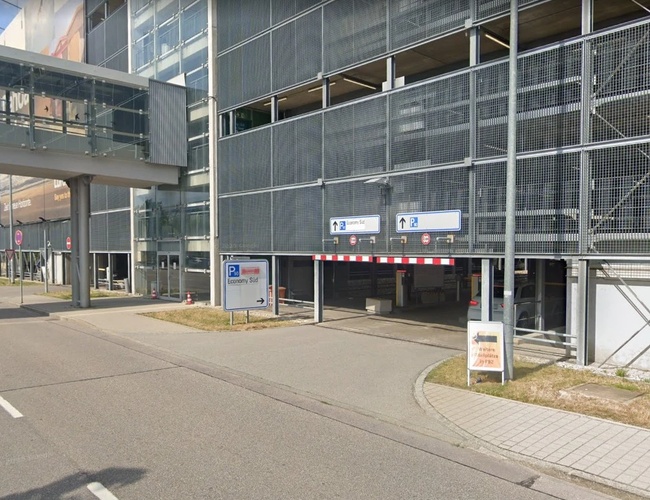 Wjazd do parkingu wielopoziomowego z oznakowaniem i szlabanem.