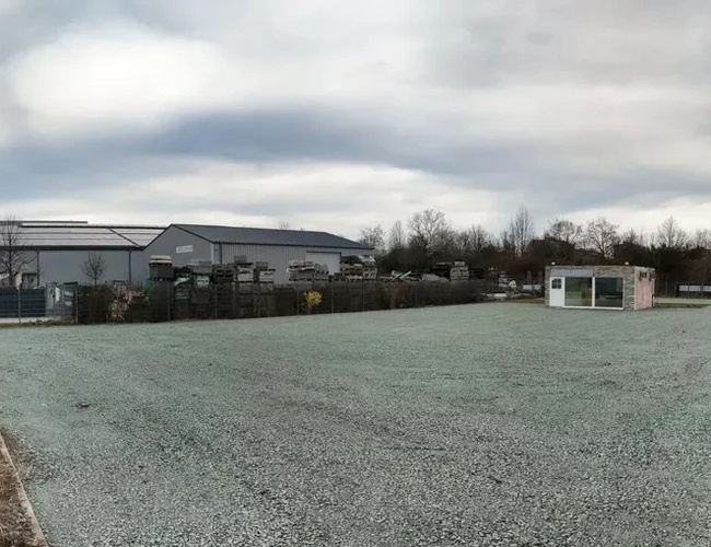 Valet de Parking de Autocares - El lugar de estacionamiento está cercado y vacío. Al fondo hay un edificio industrial y árboles.