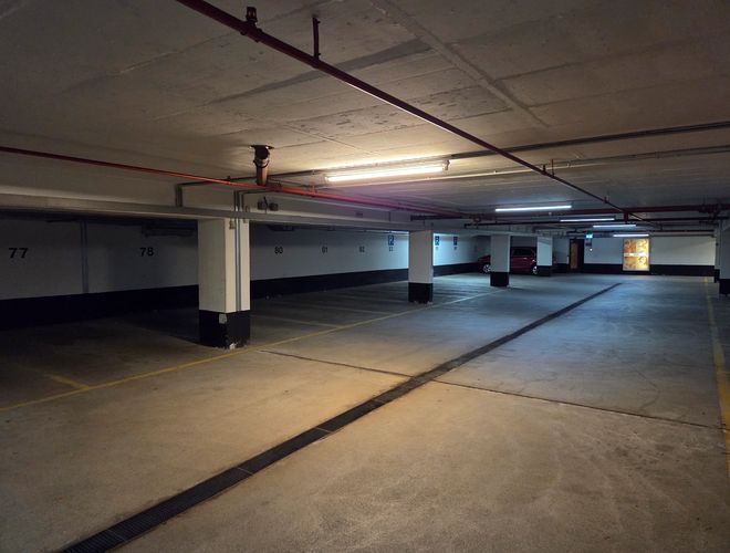 Az Atomis Hotel Munich Airport Parking Fedett - Mélygarázs jól van megvilágítva. Jelölt parkolóhelyek állnak rendelkezésre. Látható egy autó a háttérben.