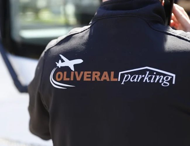 Oliveral Parking - Osoba stoi tyłem w kurtce z logo. Widać część autobusu w tle.