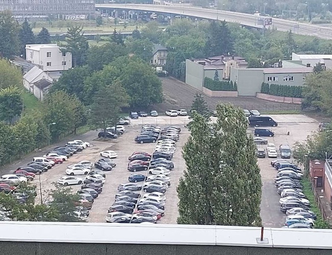 Parking Smile - Duży otwarty parking z wieloma samochodami. Teren jest otoczony drzewami i budynkami.