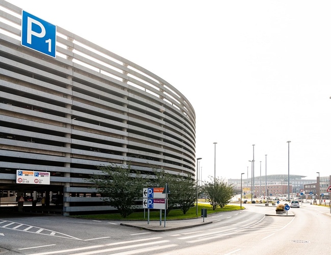 Wielopoziomowy parking P1 z oznakowaniem, zlokalizowany przy terminalu lotniska, z drogą dojazdową i wejściem dla pieszych.
