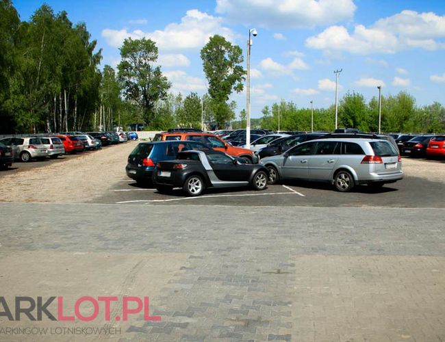 Aparcamiento P38 – El área está abierta y espaciosa. Los coches están en filas ordenadas. Al fondo hay árboles y farolas.