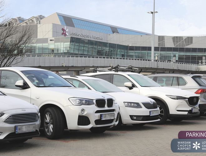 Oficjalny Parking lotniska P4 – Na parkingu stoją białe samochody. W tle widoczny jest budynek lotniska. Atmosfera jest spokojna i uporządkowana.
