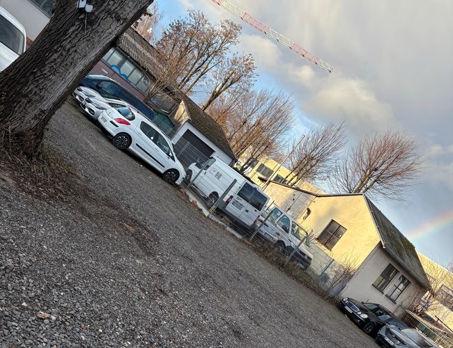 Parking ParkPoint24 Valet - Plac jest żwirowy i nieogrodzony. Stoi na nim jeden samochód. W tle widoczne są budynki.