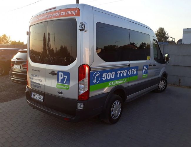 Parking P7 – Bus czeka na klientów obok samochodów. Jest zarezerwowany dla gości parkingu. Pozostałe auta stoją w tle obok płotu.