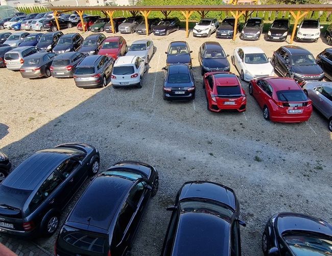 Aparcamiento PARK4YOU - El terreno es de grava y está lleno de coches. Los vehículos están estacionados en filas. Algunas plazas están cubiertas.