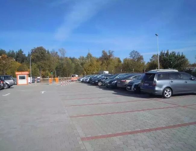 Aparcamiento Naranja Modlin - En el aparcamiento hay coches estacionados. Al fondo se puede ver la naturaleza y un cielo despejado.