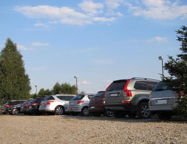 Parking Auto Park – widoczne są samochody zaparkowane na żwirowym placu. Obok rosną drzewa. W tle widać latarnie.