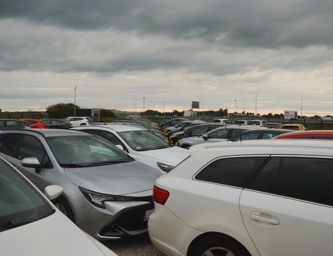 Royal Parking – Na obrázku sú viditeľné zaparkované autá. Nebo je zamračené. Pozemok je ohradený a priestranný.