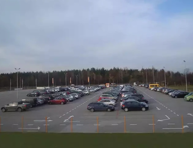 Oranžové parkovisko Modlin - Parkovisko je plné áut. Pozemok je ohradený a osvetlený. V pozadí sú stromy.