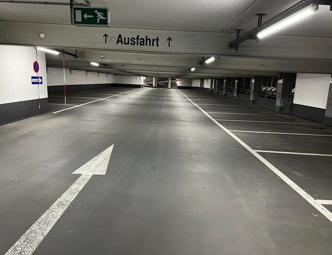 Parking Park2Travel Valet Garage - Pusta hala parkingowa z wyraźnym oznakowaniem. Na suficie znajdują się lampy. Na podłodze widać strzałkę kierunkową.