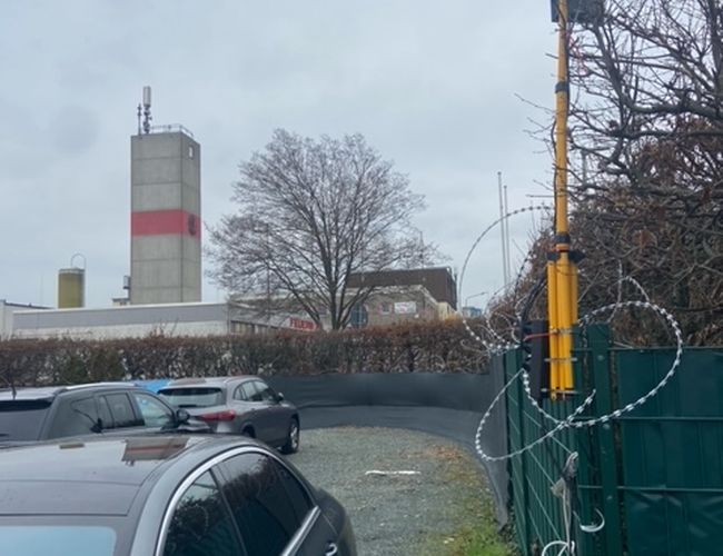 Parking Park-Box-Frankfurt Valet - Teren jest ogrodzony i oświetlony. Auta stoją zaparkowane blisko siebie. W tle widać drzewa i budynek.