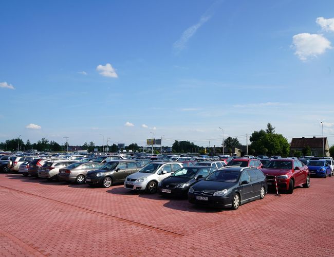 MEGA Parking - un gran espacio abierto lleno de coches. Los adoquines rojos cubren la superficie. A lo lejos se pueden ver árboles y edificios.