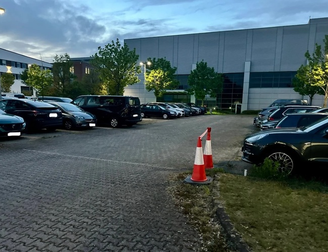 Parkovisko FRAir Valet Park Service – veľa zaparkovaných áut. Parkovisko je dobre osvetlené lampami. Na pozadí sú viditeľné stromy a budova.