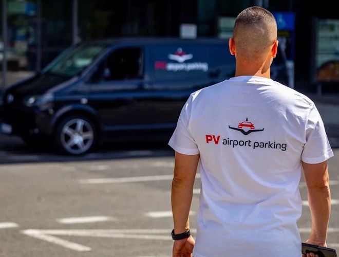 Pracownik PV Airport Parking spacerujący po terenie parkingu lotniskowego, widoczny na tle samochodu transferowego z oznaczeniem parkingu.