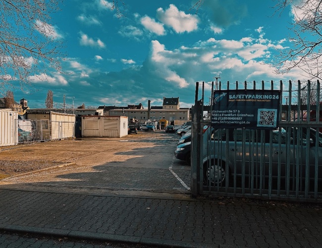 Bezpečnosť parkovania parking24 VALET - Územie je ohradené. Na dvore stojí niekoľko áut. V pozadí sú kontajnery a budovy.