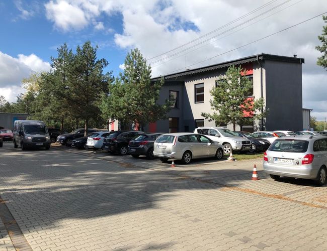 Parking A1 – na zdjęciu widoczne są zaparkowane samochody. Teren otaczają drzewa i budynek. Parking ma wyłożoną kostkę brukową.