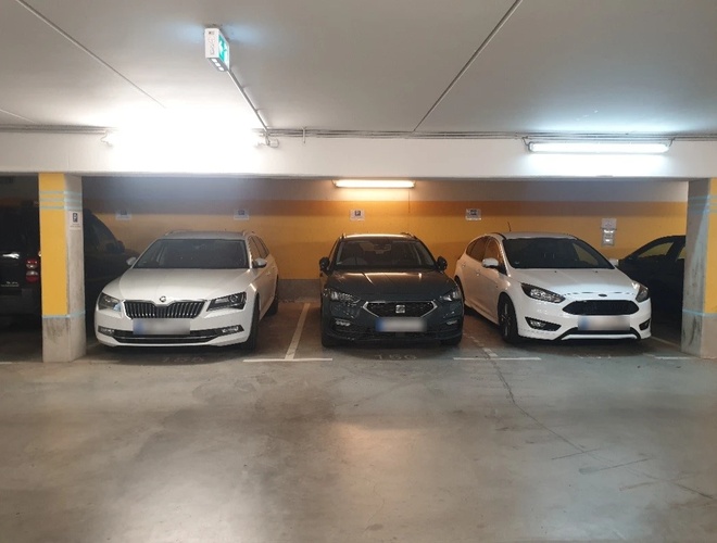 Trzy zaparkowane samochody na podziemnym parkingu, żółta ściana i sufit z oświetleniem LED.