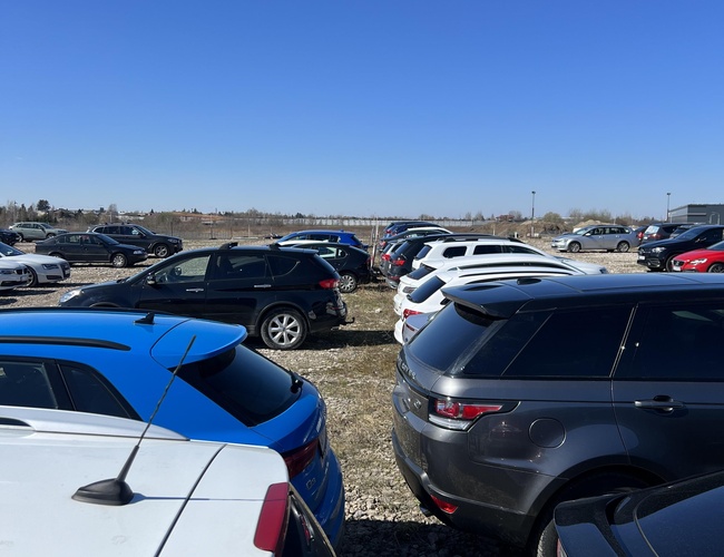 P12 Estacionamiento - Los coches están estacionados cerca unos de otros en un área de grava. En el horizonte se ve un espacio abierto.