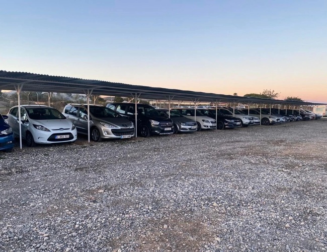 Najlepšie parkovisko v Alicante s krytým valet – Automobily stoja pod prístreškom. Parkovisko sa nachádza na neupravenej ploche.