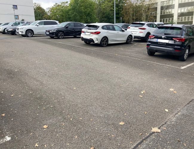 Parking Stern Valet - widoczne są zaparkowane samochody. Teren parkingu jest otwarty i asfaltowy. W tle rosną drzewa i stoją budynki.