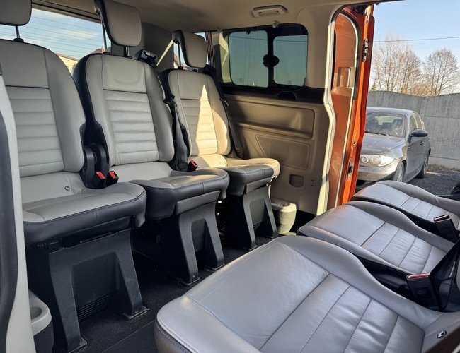 Parking Wings - Interior del vehículo, se pueden ver tres filas de asientos. Las puertas laterales están abiertas, al fondo un coche gris.