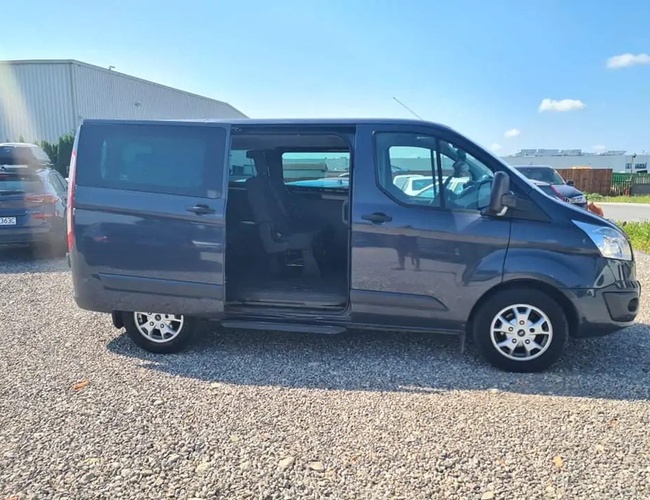 Parkovisko Dominik - Autobus zaparkovaný na štrkovom nádvorí. Bočné dvere sú otvorené. V pozadí sú ďalšie autá.