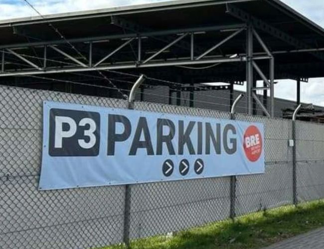 Baner z oznaczeniem „P3 PARKING” umieszczony na ogrodzeniu przy wjeździe na teren parkingu. W tle widoczna jest zadaszona konstrukcja parkingowa.