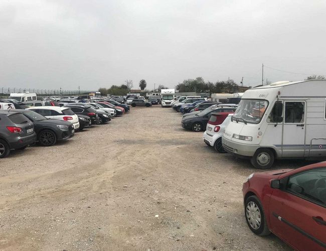 Parking Drimo Park Valet – Teren jest nieutwardzony i otwarty. Stoją tam liczne samochody oraz kamper. Parking jest przestronny i niezadaszony.