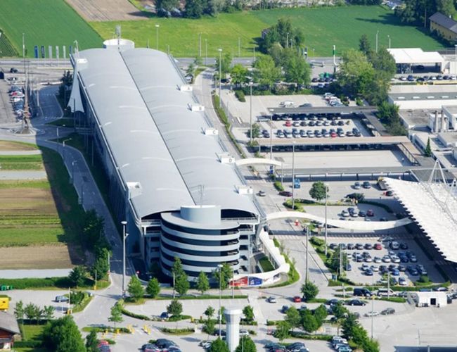Widok z lotu ptaka na kompleks budynków z wielopoziomowym parkingiem i parkingami terenowymi. Obiekt otaczają drogi wewnętrzne oraz tereny zielone.