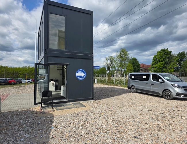Premium parkovisko – Na štrkovom povrchu stojí sivý kontajner. Vedľa neho je zaparkované sivé auto. Po pravici sú viditeľné stromy a niekoľko áut.