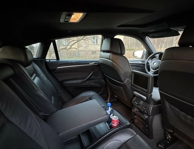 Parking MB Park - Wnętrze samochodu z czarną skórzaną tapicerką. Na środku leży butelka wody i puszka napoju. Szerokie siedzenia z oparciem.