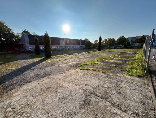 Park, Shuttle & Fly MUC – Zufahrtsstraße. Im Hintergrund Parkplätze, Bäume und ein Gebäude.
