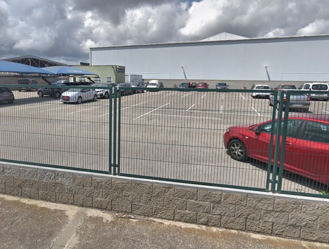 Parkovisko Park and Greet Valet - ohradený priestor s zaparkovanými autami. V pozadí je vidieť halu s bielou strechou.
