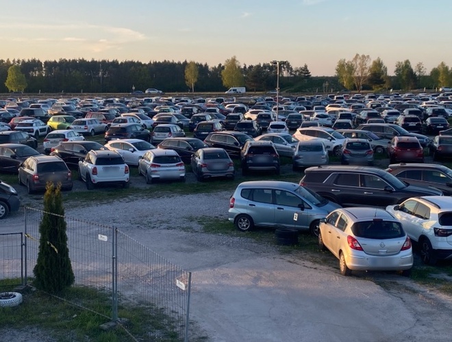 Aparcamiento debajo de los molinos - En la gran plaza hay numerosos coches. El área está cercada y es abierta. Al fondo se pueden ver árboles.