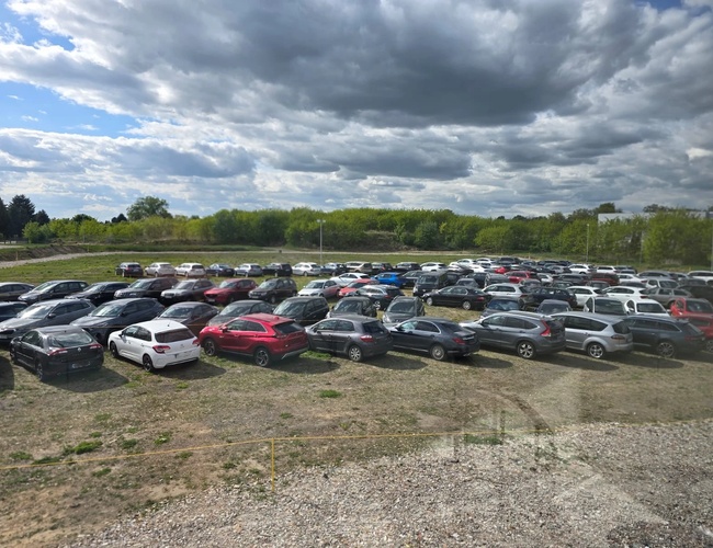 Prémiové parkovisko - Na parkovisku stojí veľa áut. Pozemok je obklopený zeleňou. Nie sú tu viditeľné žiadne ploty ani lampy.