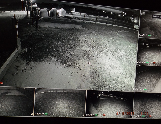 VIP Parking - ogrodzony plac monitorowany nocą. W tle widać oświetlenie. Na ekranie pokazano różne ujęcia z kamer.