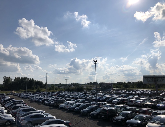 Parkovisko A1 Rondo - Veľké parkovisko plné áut. Areál je ohradený a osvetlený. Na obzore sú stromy a billboard.