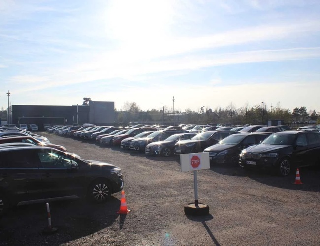 ArtLot 2 - Gran aparcamiento con coches estacionados. Se puede ver un cartel de "Alto". El aparcamiento no está cercado, ubicado al aire libre.