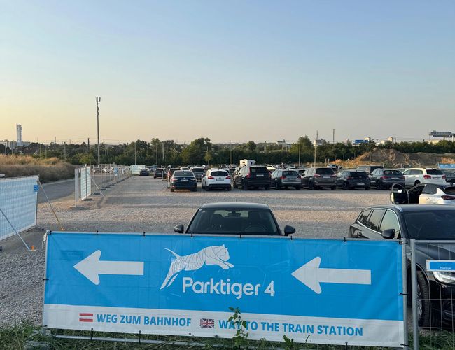 Niebieski baner ukazujący białą strzałkę, wskazującą kierunek do stacji pociągów w celu dotarcia na lotnisko z parkingu.