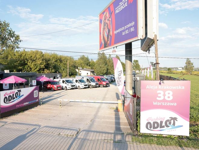 Parking Odlot - Na parkingu stoją zaparkowane samochody i dwa duże pojazdy firmowe. Teren jest ogrodzony i zamknięty szlabanem.